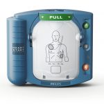 Närbild av Philips HeartStart HS1, en blåturkos hjärtstartare med symboler och knappar på vit bakgrund, förberedd för att ge livräddande behandling.